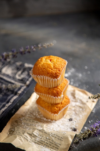 Una vista frontale deliziose torte con fiori viola sullo zucchero dolce del biscotto del tè del biscotto della tavola grigia
