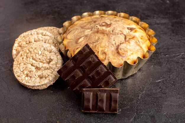 Una vista frontale dolce torta rotonda squisita deliziosa all'interno della tortiera insieme a barrette di cioccolato e patatine fritte sullo sfondo grigio biscotto zucchero biscotto