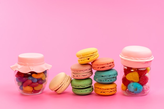 Una vista frontale francese macarons colorati insieme a caramelle multicolori all'interno di lattine su rosa, pasticceria biscotto torta