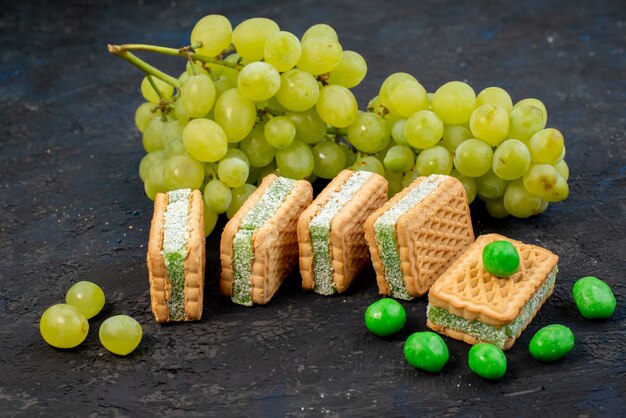 Una vista frontale fresca uva verde aspro succosa e pastosa con i biscotti sullo sfondo scuro frutta matura pianta verde