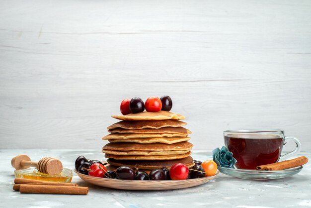 Una vista frontale frittelle con ciliegie all'interno del piatto con cannella e tè sullo sfondo scuro biscotto torta di frutta cuocere