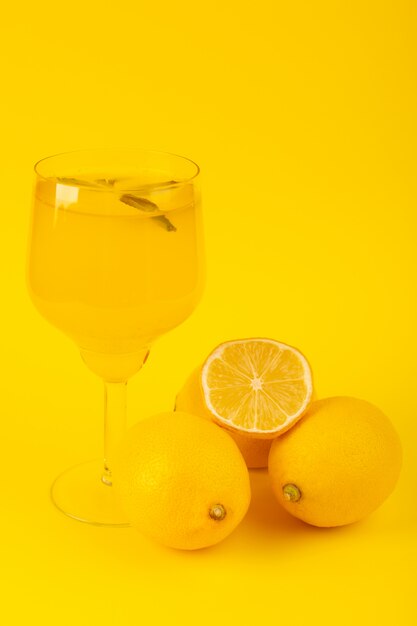 Una vista frontale giallo limoni freschi freschi maturi interi e affettati con bevanda al limone all'interno di vetro frutta isolato su sfondo giallo colore di agrumi