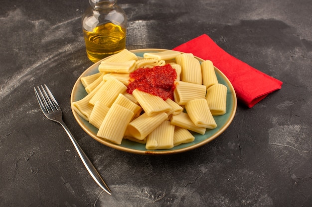 Una vista frontale ha cucinato la pasta italiana con salsa di pomodoro all'interno del piatto sul pasto di cibo italiano di pasta da tavola grigia