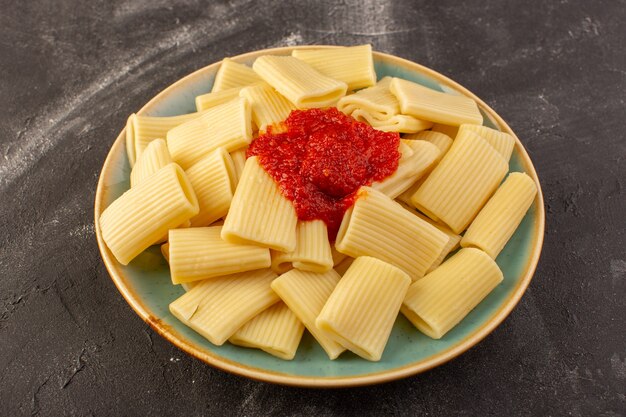 Una vista frontale ha cucinato la pasta italiana con salsa di pomodoro all'interno del piatto sul pasto di cibo italiano di pasta da tavola grigia