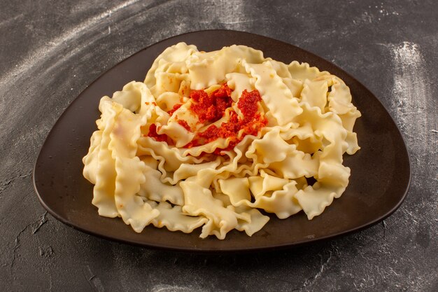 Una vista frontale ha cucinato la pasta italiana con salsa di pomodoro all'interno del piatto sulla superficie grigia