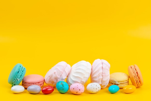 Una vista frontale meringhe e macarons deliziosi e dolci su caramelle arcobaleno di colore giallo