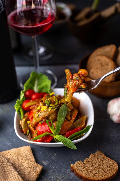 Una vista frontale patate fritte insieme con verdure a fette foglie verdi all'interno del piatto bianco insieme a patatine vino rosso sulla scrivania grigia vitamine verdure