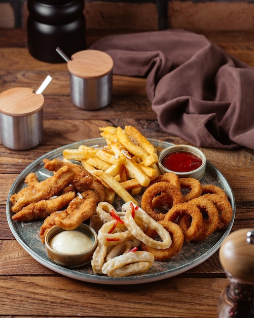 Una vista frontale patatine fritte con ali di pollo fritte e anelli di cipolla con ketchup sulla patata pasto cibo scrivania in legno marrone