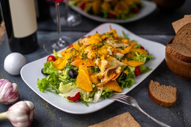 Una vista frontale patatine fritte con verdure a fette verdi all'interno del piatto bianco salato pepato insieme con patatine di vino rosso sui piatti della cena scrivania grigia