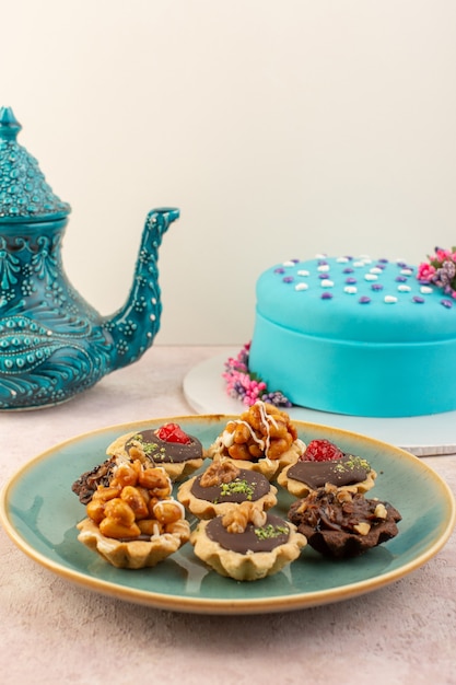 Una vista frontale piccoli dolci al cioccolato all'interno del piatto con torta di compleanno blu sullo scrittorio rosa