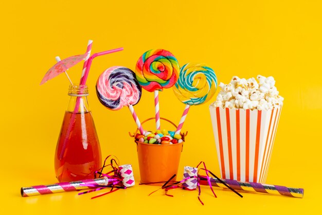 Una vista frontale popcorn e cocktail alongw con caramelle colorate e lecca-lecca su giallo