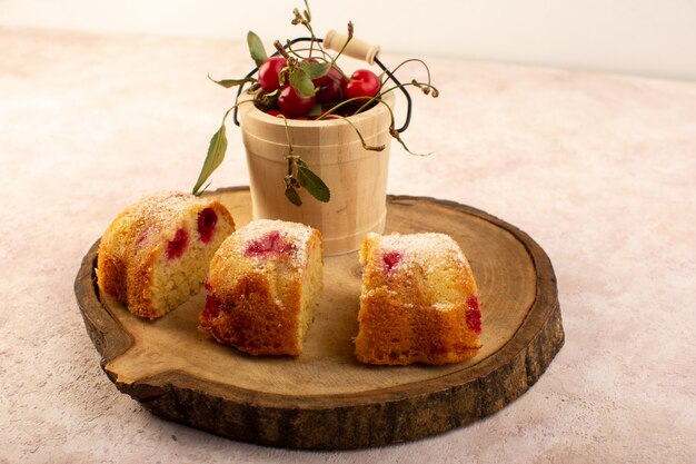 Una vista frontale torta di frutta al forno deliziosa affettata con ciliegie rosse all'interno e zucchero in polvere sullo scrittorio di legno con ciliegie fresche sul rosa