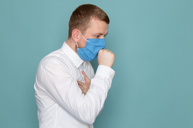 Una vista frontale tosse giovane in camicia bianca con maschera blu sullo spazio blu