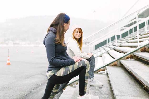 Una vista laterale di due atleta femminile che allunga la sua gamba sulla scala in inverno