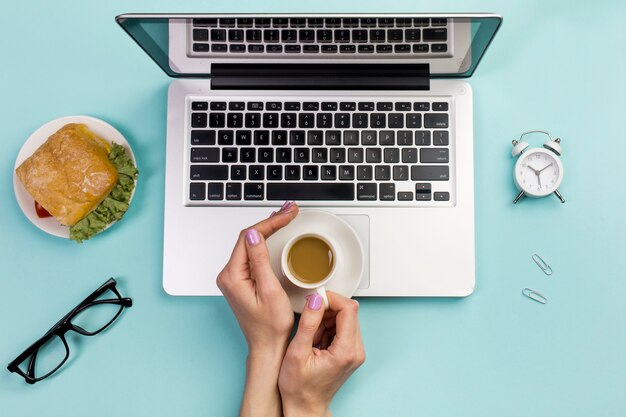 Una vista sopraelevata della tazza di caffè della tenuta della mano di una donna di affari sopra il computer portatile contro il contesto blu