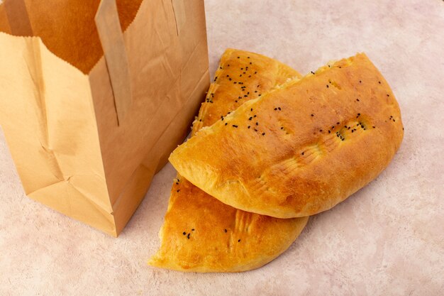 Una vista superiore del pane cotto caldo gustoso metà fresca affettata all'interno e all'esterno dei pacchetti di carta sul rosa