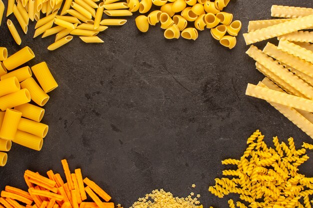 Una vista superiore della pasta cruda gialla differente formata ha isolato poco e lungo sugli spaghetti scuri dell'Italia dell'alimento del pasto del fondo