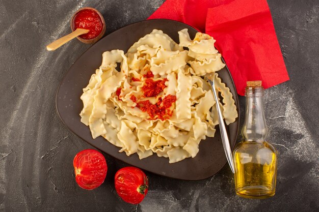 Una vista superiore ha cucinato la pasta italiana con salsa di pomodoro all'interno del piatto sulla pasta italiana del pasto dell'alimento della tavola grigia