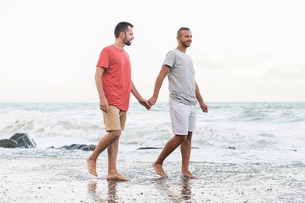 Uomini del colpo pieno che camminano sulla spiaggia