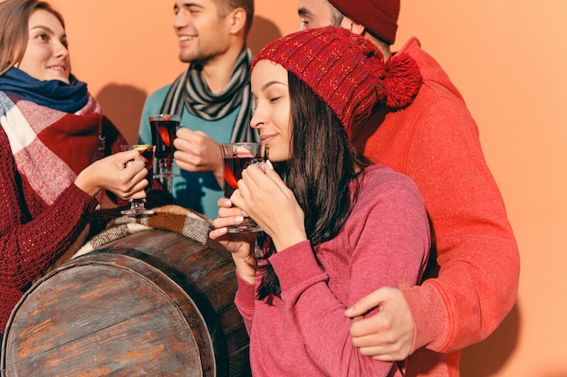 Uomini e donne europei sorridenti durante il servizio fotografico del partito. ragazzi in posa come amici allo studio fest con bicchieri di vino con vin brulè caldo in primo piano.