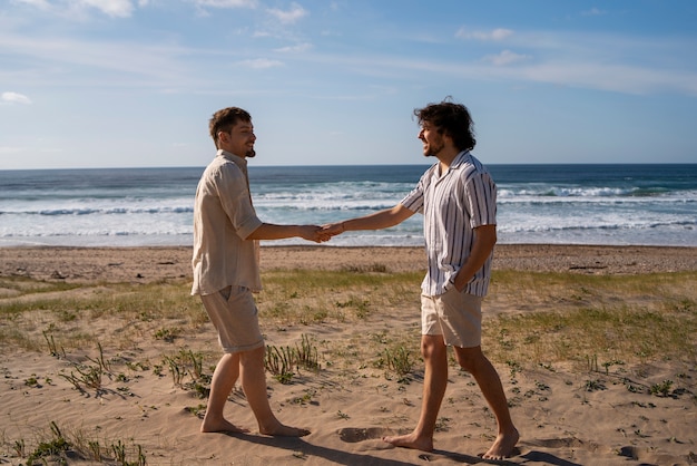 Uomini gay a tutto campo che si tengono per mano in spiaggia