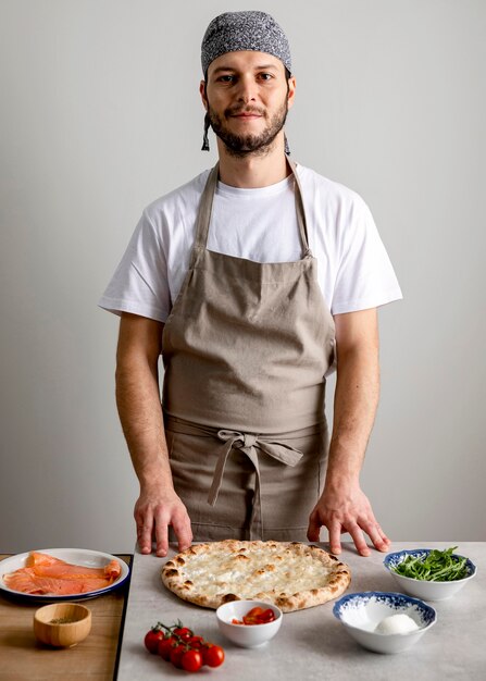 Uomo a metà colpo in piedi vicino a pasta per pizza al forno con ingredienti