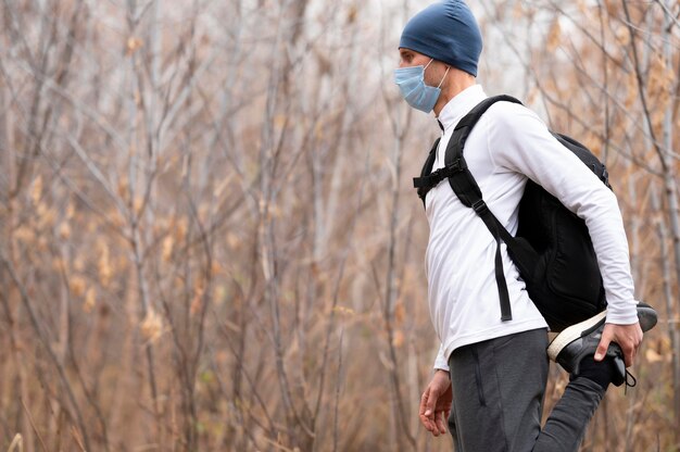 Uomo a metà tiro con maschera facciale nel bosco che allunga le gambe