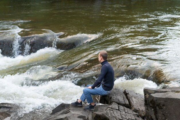 Uomo a tutto campo seduto in riva al fiume