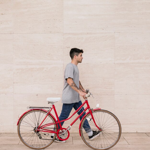 Uomo adolescente che cammina con la sua bicicletta vicino al muro