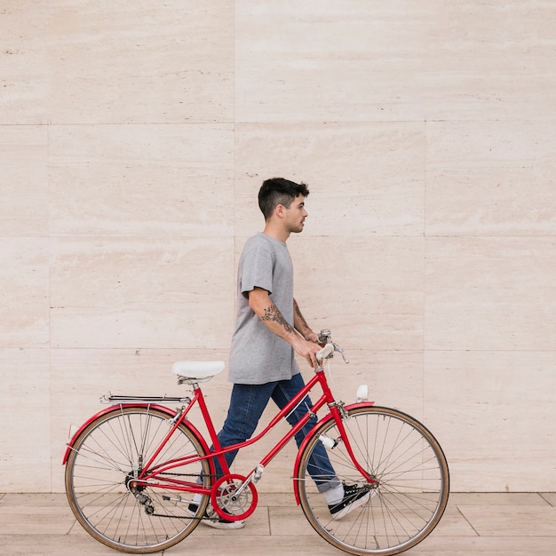 Uomo adolescente che cammina con la sua bicicletta vicino al muro