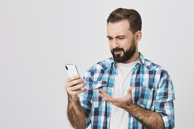 Uomo adulto deluso confuso guardando lo schermo dello smartphone