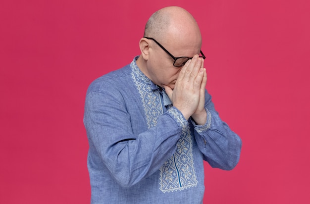 Uomo adulto deluso in camicia blu con gli occhiali che si mette le mani sul naso