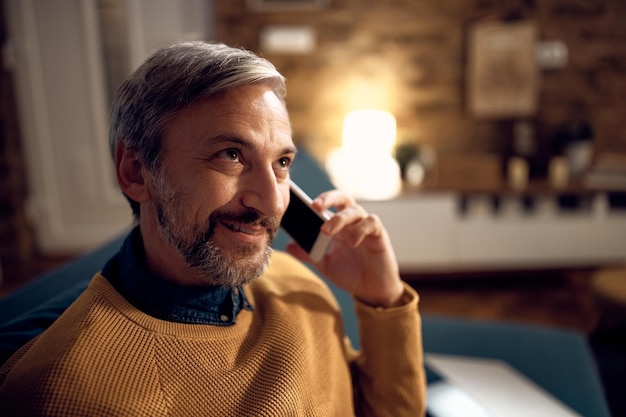 Uomo adulto metà sorridente che parla al telefono di notte a casa