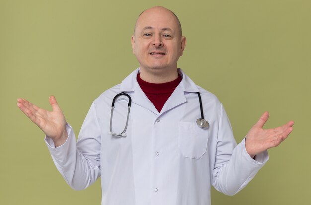 Uomo adulto sorridente in uniforme da medico con stetoscopio che tiene le mani aperte