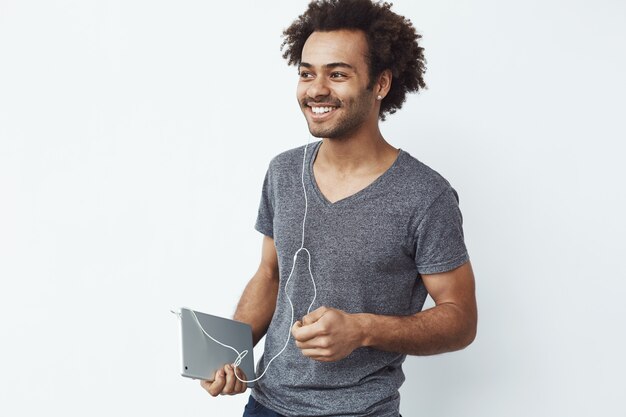 Uomo africano allegro in compressa sorridente della tenuta delle cuffie.