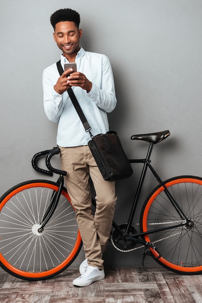 Uomo africano che sta bicicletta vicina che chiacchiera dal telefono.