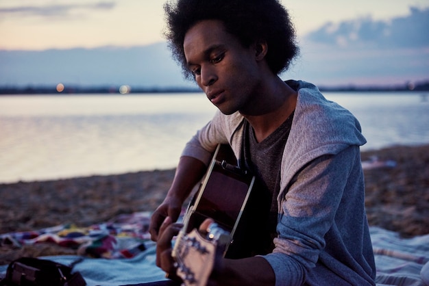 Uomo africano che suona la chitarra sulla spiaggia di notte