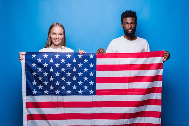 Uomo africano con donna caucasica che tiene bandiera americana isolata sulla parete blu