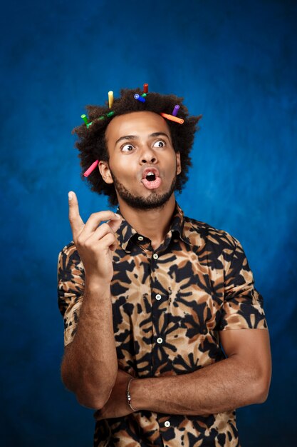 Uomo africano con gli indicatori in capelli che pensa sopra la parete blu.