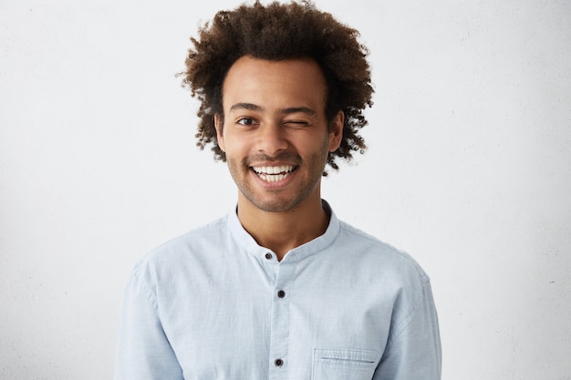 Uomo africano divertente con capelli ricci folti che sbatte le palpebre con un ampio sorriso caldo