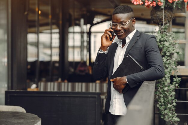 Uomo africano. Ragazzo in abito nero. Maschio con un telefono cellulare. Uomo d'affari in ufficio.