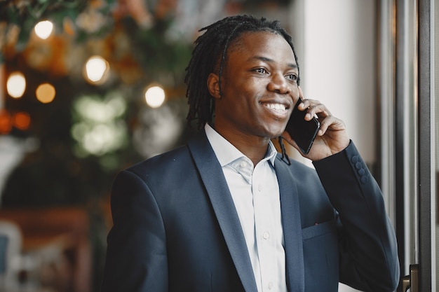 Uomo africano. Ragazzo in abito nero. Maschio con un telefono cellulare.