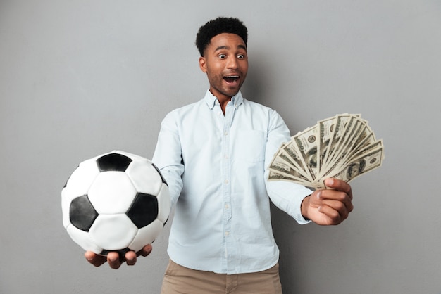 Uomo africano sorridente felice che mostra le banconote dei soldi e di calcio