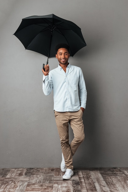 Uomo africano sorridente felice che sta con l'ombrello aperto