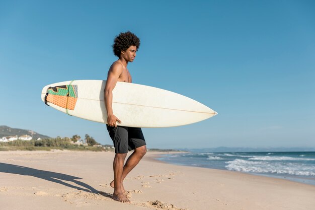 Uomo afroamericano adulto che prepara per praticare il surfing