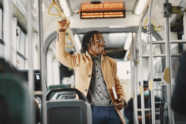 Uomo afroamericano che guida nel bus della città. Ragazzo con un cappotto marrone. Uomo con il taccuino.