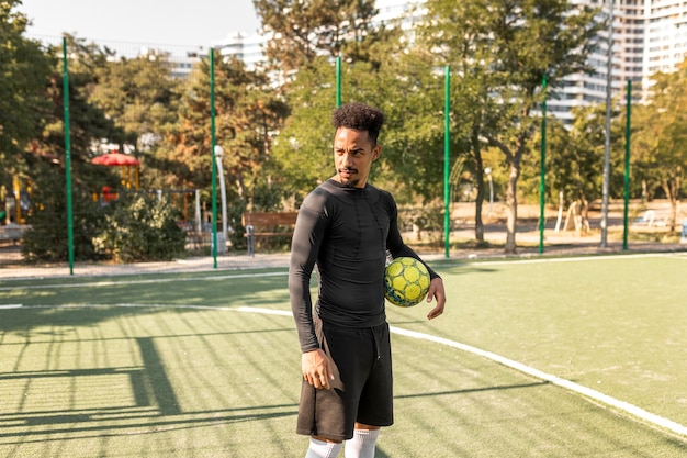 Uomo afroamericano del colpo lungo che posa con un pallone da calcio