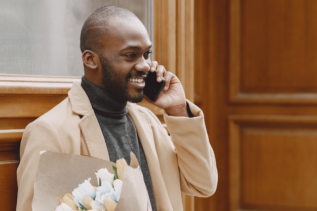 Uomo afroamericano in una città. Ragazzo che tiene il mazzo di fiori. Maschio in un cappotto marrone.