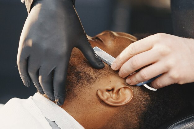 Uomo afroamericano. Ragazzo seduto su una sedia. Il barbiere lavora con la barba.