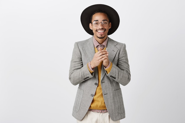 Uomo afroamericano sorridente grato bello che tiene le mani insieme e che guarda con apprezzamento